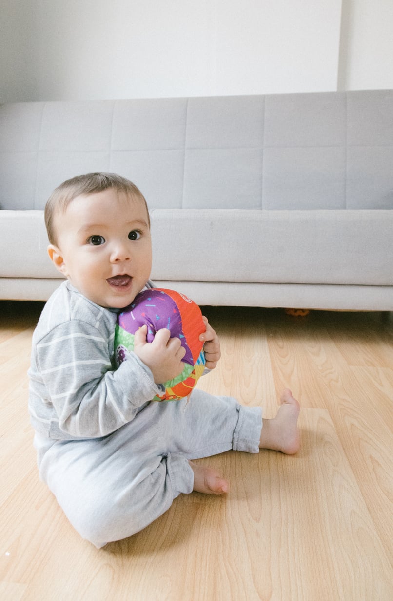 Child Holding a Ball Sitting on Wooden Floor